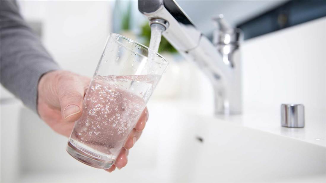 Person filling a glass of water from a kitchen faucet